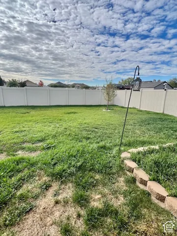 Expansive backyard featuring a white vinyl privacy fence, a stone-bordered garden bed, and a mature tree