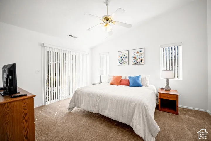 Vaulted ceilings featuring a central white ceiling fan with multi-light fixture, sliding glass patio door with vertical blinds, and neutral carpeting