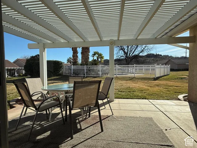 Covered concrete patio featuring a slatted pergola, enclosed backyard, white vinyl fencing, and distant mountain topography