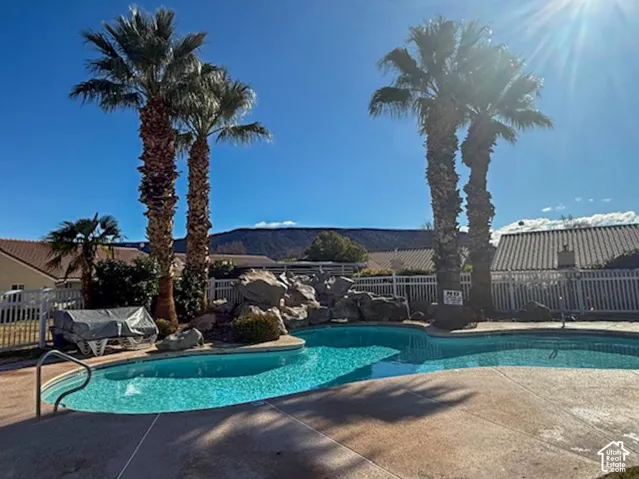 Swimming pool featuring a rock waterfall, concrete decking, mature palm trees, and mountain backdrop