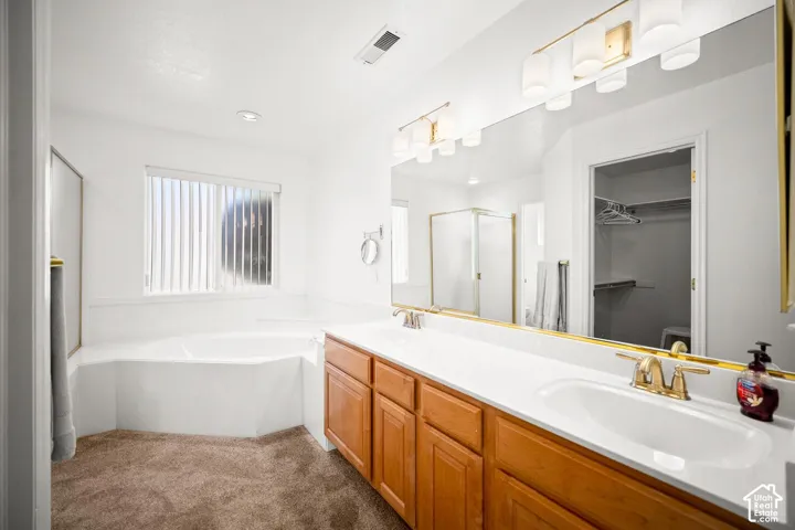 Dual-sink vanity with light wood-finish cabinetry, solid-surface countertop, built-in soaking tub, full-width wall mirror, and multi-bulb vanity lighting