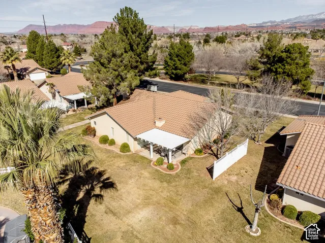 Aerial perspective featuring a tile roof, covered patio, white privacy fencing, and mature landscaping set against a mountain backdrop