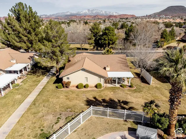 Stucco exterior featuring a clay tile roof, covered patio, white vinyl fencing, and mature palm landscaping with mountain backdrop