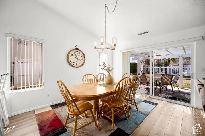 Dining area featuring light-toned wood-finish flooring, a multi-bulb chandelier, and sliding glass doors opening to a covered patio