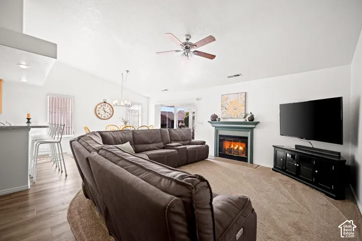 Vaulted ceilings, fireplace with a decorative mantel, ceiling fan with integrated lighting, wood-finish flooring, and a breakfast bar with stone-finish countertops