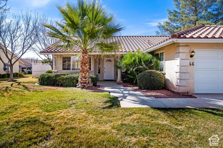 Stucco exterior featuring a clay tile roof, decorative stone quoins, a concrete walkway, and landscaped grounds with mature palm trees