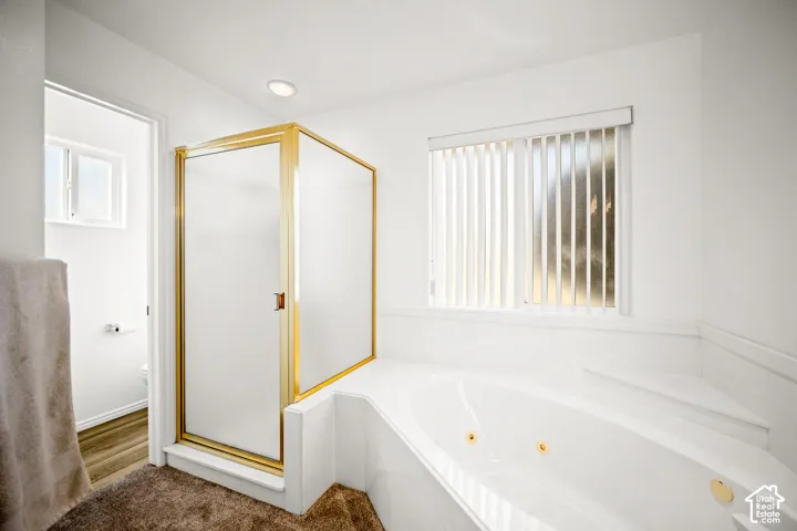 Soaking tub with integrated jets and gold-tone hardware, enclosed shower with gold-tone frame, recessed lighting, and vertical window blinds