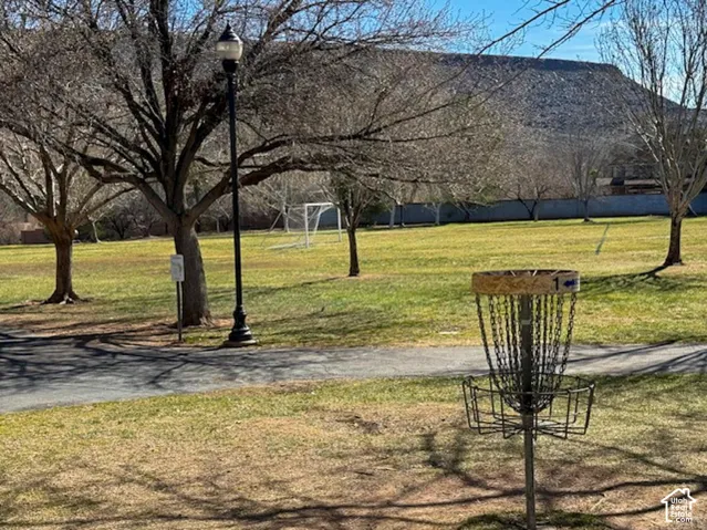 Expansive lawn featuring mature trees, paved pathway, pole-mounted lighting, and permanent disc golf infrastructure with a mountain backdrop