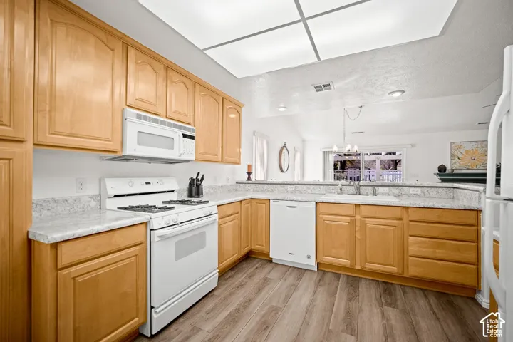 Kitchen featuring light-tone wood cabinetry, stone-finish countertops, white appliances, and wood-finish flooring