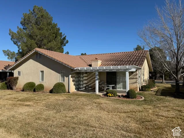 Stucco exterior featuring a clay tile roof, covered patio with a white pergola, and landscaped garden beds