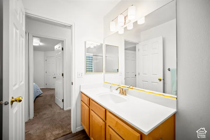 Bathroom vanity featuring a solid surface countertop, integrated sink with metallic faucet, light wood-finish cabinetry, and a large wall-mounted mirror with multi-bulb overhead lighting