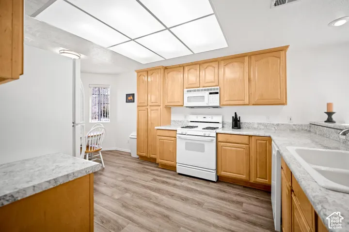 Kitchen featuring wood cabinetry, stone-finish countertops, wood-finish flooring, integrated white appliances, and a large-format recessed ceiling light