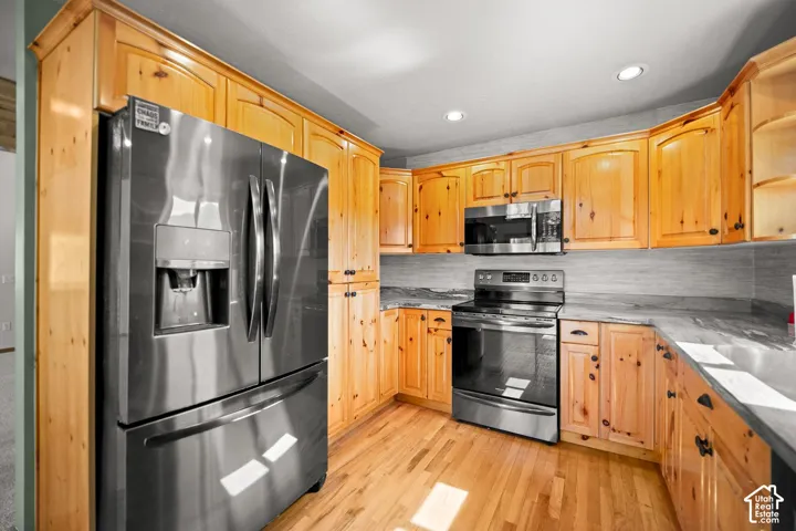 Kitchen featuring knotty wood cabinetry, stone-finish countertops, stainless steel appliances, and wood-finish flooring