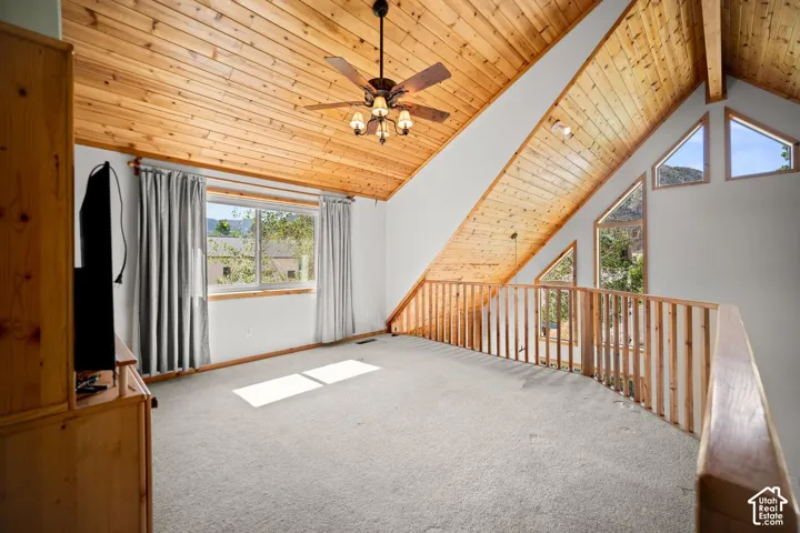 Vaulted ceiling with tongue-and-groove wood paneling, wood-slat railing, geometric windows, and a central ceiling fan