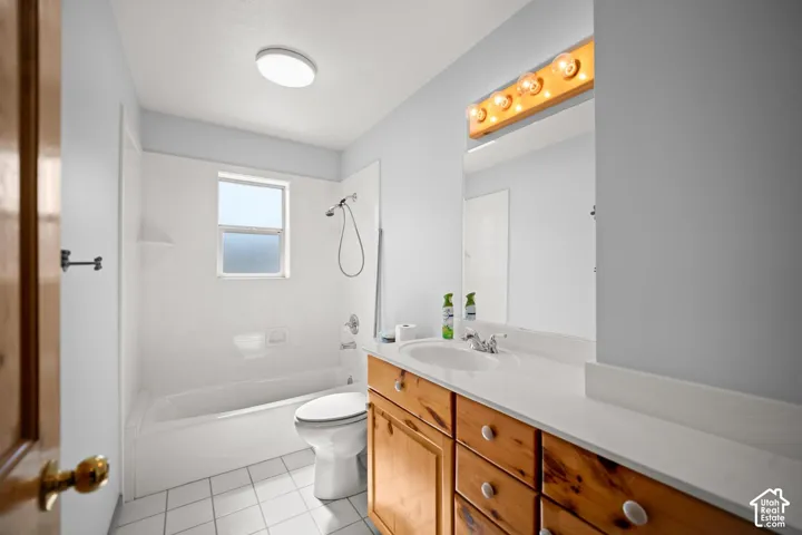 Bathroom featuring a bathtub and shower combination, a wooden vanity with integrated countertop sink, a large wall-mounted mirror, and tile flooring