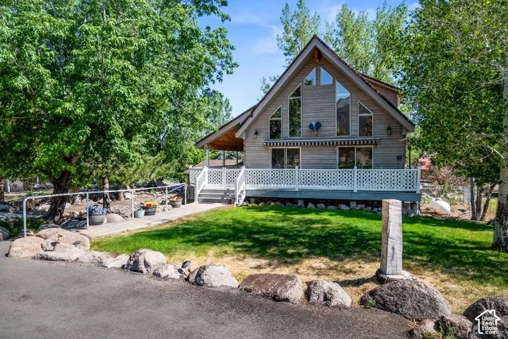 A-frame exterior featuring horizontal wood siding, floor-to-ceiling geometric windows, a wrap-around deck with lattice railing, and a concrete pathway