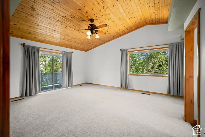 Vaulted ceiling featuring wood-plank paneling, sliding glass door, and a ceiling fan with integrated lighting