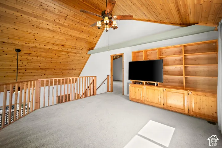 Vaulted ceiling with natural wood-plank paneling, integrated wood-finish built-in cabinetry and shelving, and wooden balustrade railing