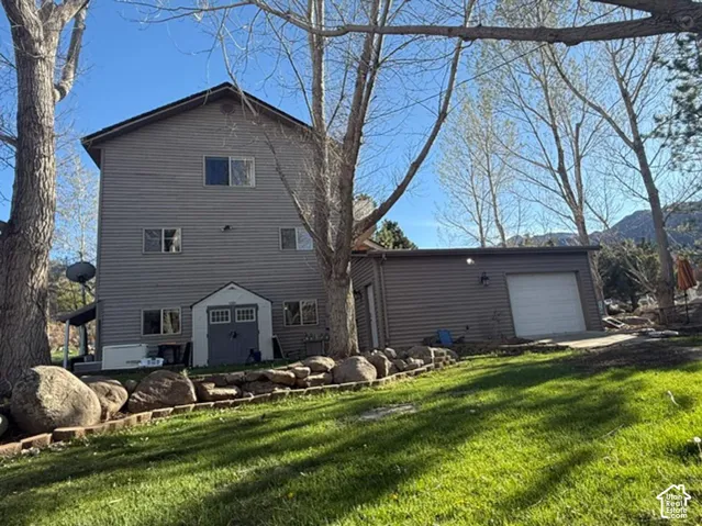 Three-story residence featuring horizontal lap siding, an attached garage, a detached storage structure, and rock-lined landscaping set against a mountainous backdrop