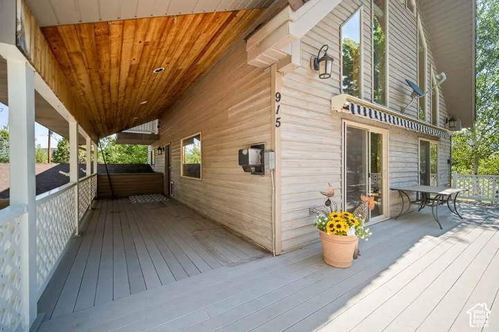 Expansive exterior deck featuring a wood-plank ceiling, white lattice railing, horizontal siding, and multiple sliding glass doors