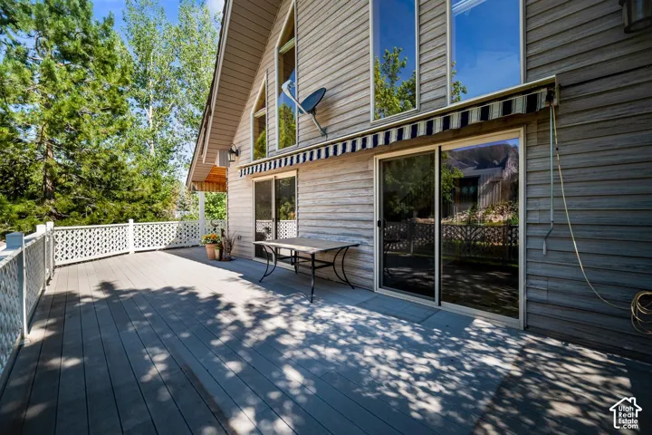 Spacious wood-finish deck with white lattice railings, vertical siding exterior, multi-story windows, and a retractable fabric awning