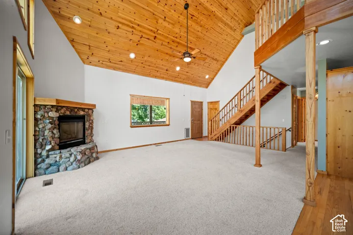 Vaulted ceiling with exposed wood planking, floor-to-ceiling stone fireplace, open timber staircase with wooden railing, and recessed lighting