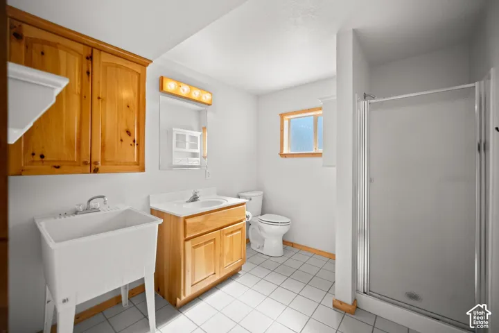 Bathroom featuring a white utility sink, wood-finish cabinetry, a shower stall with a glass door, and tiled flooring