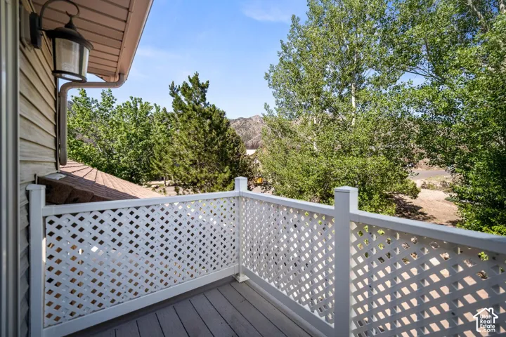 Private balcony featuring wood-finish decking, white lattice railing, and wall-mounted exterior lighting