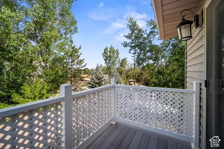 Elevated balcony featuring horizontal-plank composite decking, white lattice railings, and an attached wall-mounted exterior sconce