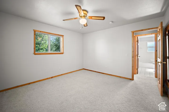 Interior space featuring neutral wall-to-wall carpeting, natural wood window trim, a multi-blade ceiling fan, and six-panel interior wooden doors