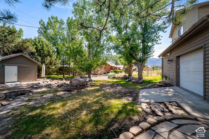 Outdoor space featuring natural stone hardscaping, a detached storage structure, mature trees, and mountainous terrain