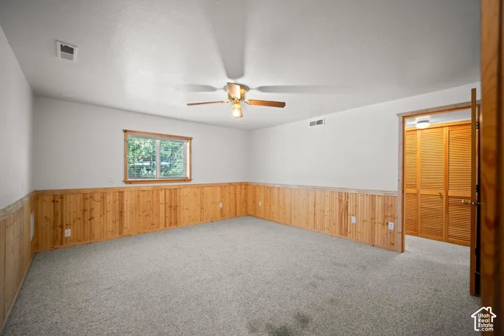 Room interior featuring natural wood wainscoting, wall-to-wall carpeting, a ceiling fan with integrated lighting, and louvered closet doors