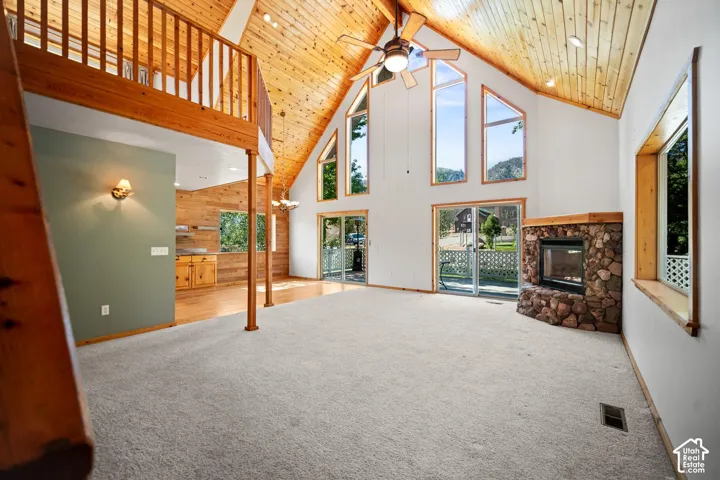 Vaulted tongue-and-groove wood ceiling, floor-to-ceiling windows, stone-surround fireplace, and wood-railing mezzanine