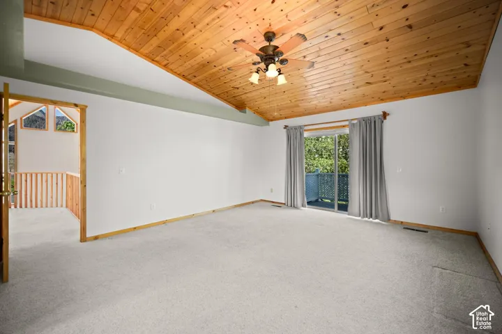 Vaulted ceiling with wood-plank paneling, integrated ceiling fan with light fixture, sliding glass door, and wooden railing