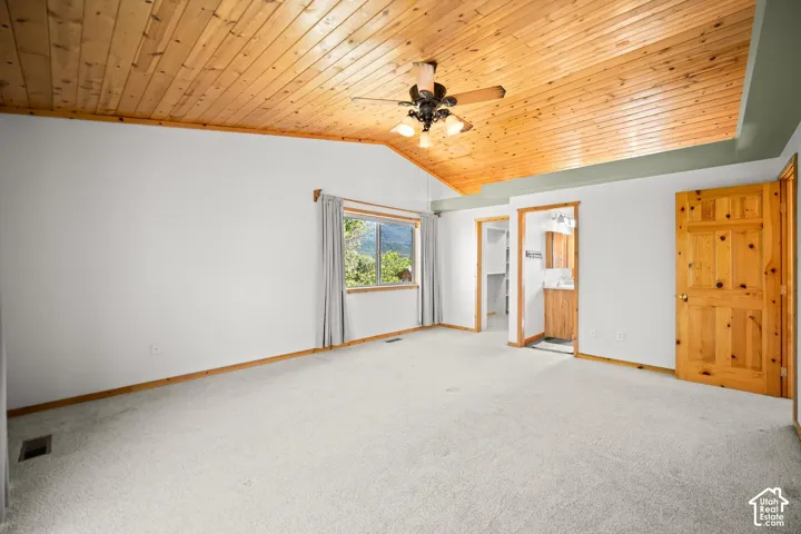 Vaulted ceiling featuring natural wood paneling, central ceiling fan with integrated lighting, neutral carpeting, and a six-panel wood door