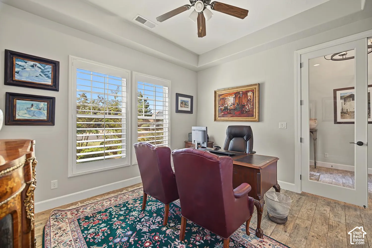Tray ceiling with central paddle fan, plantation shutters, and glass-paneled entry door featuring brushed metal hardware and tile flooring