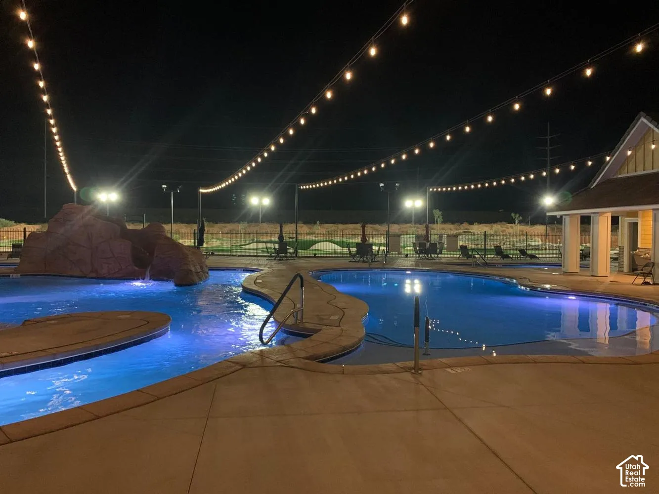Swimming pool featuring a rock waterfall feature, concrete decking, and overhead string lighting
