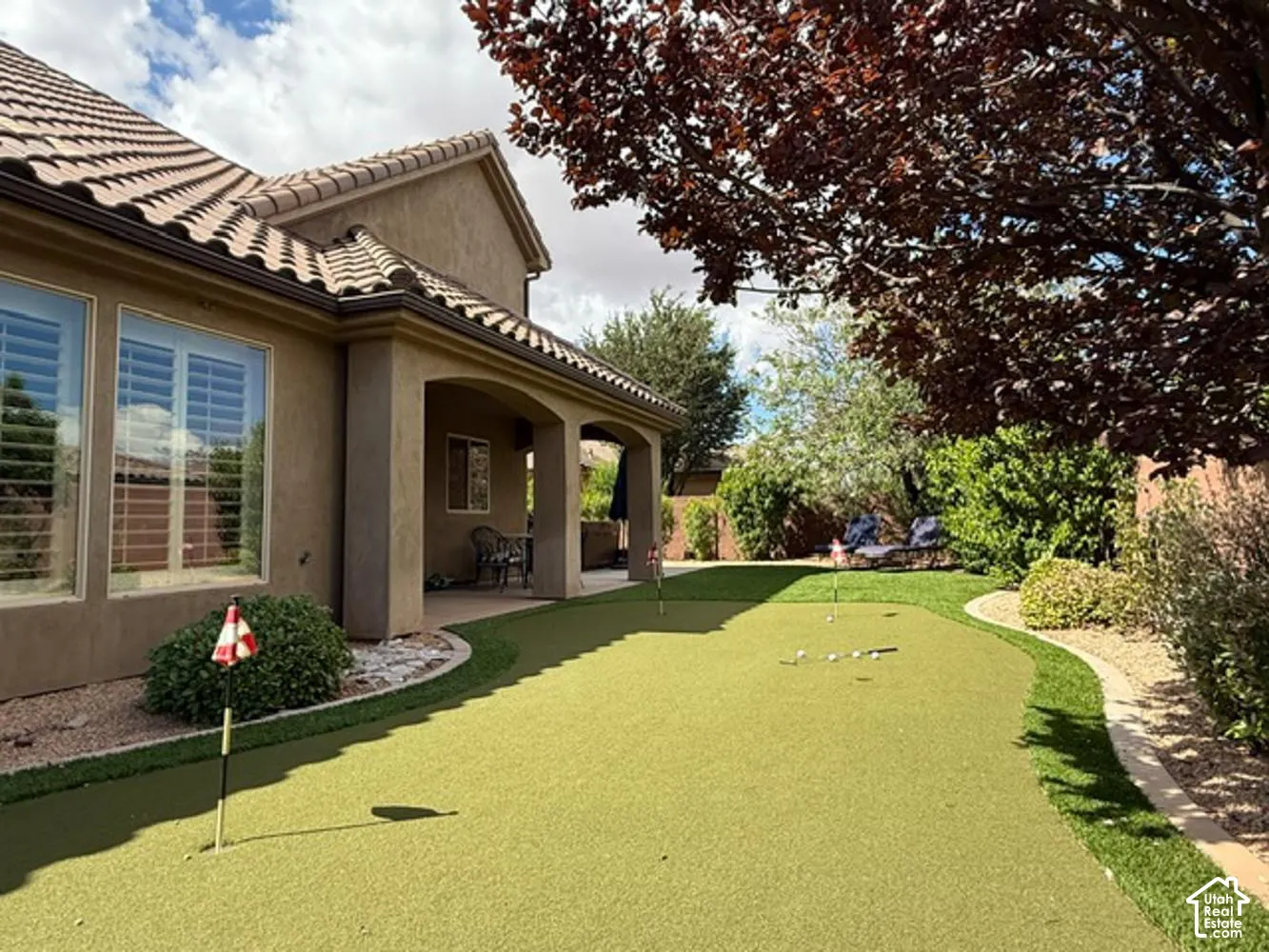 Stucco exterior featuring a covered patio, tile roof, and a professional-grade artificial turf putting green with integrated holes