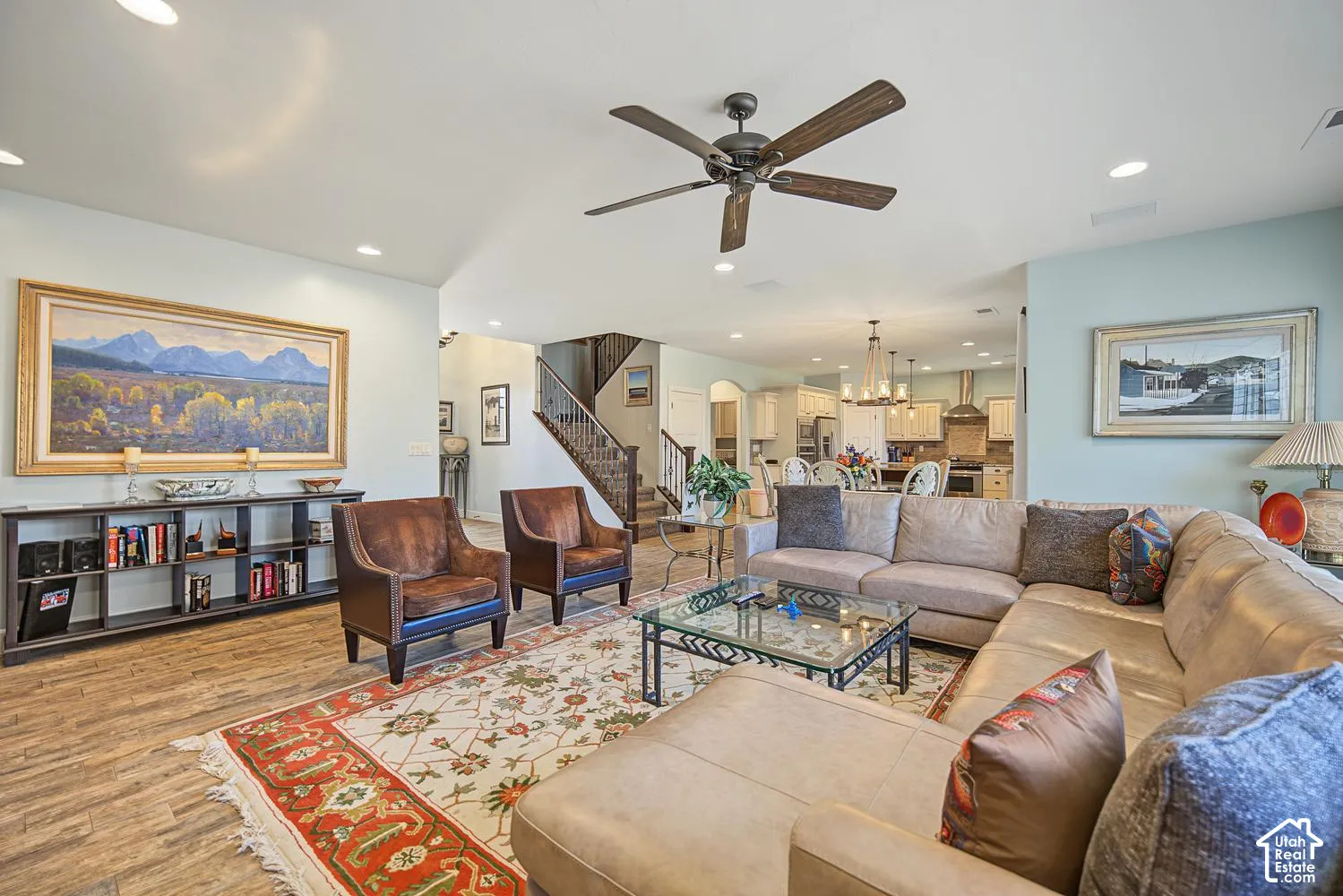 Open-concept interior featuring wood-finish flooring, recessed lighting, a ceiling fan, and a staircase with a dark wood handrail and iron balusters