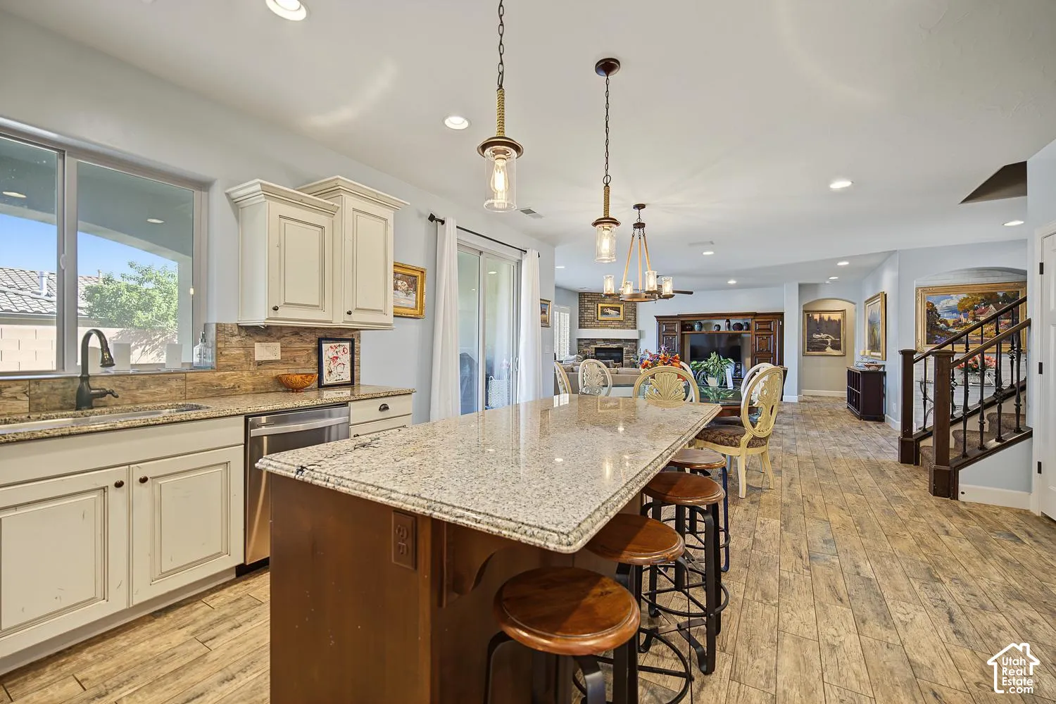 Kitchen featuring an island with a stone countertop, wood-finish flooring, custom cabinetry, stainless steel dishwasher, and pendant lighting