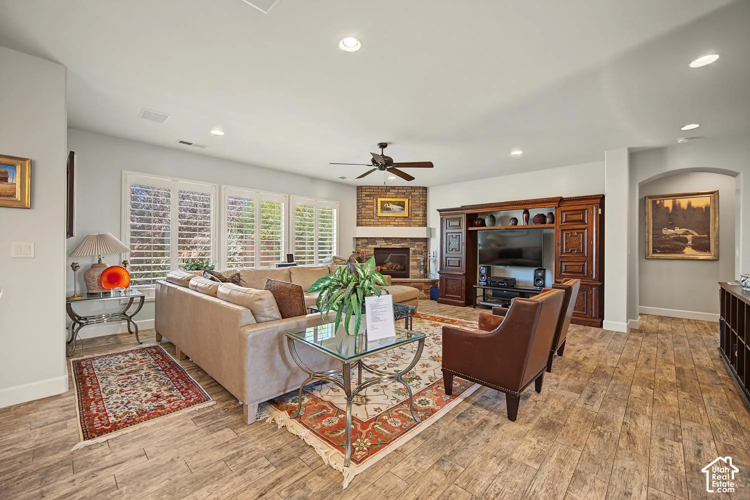 Wood-finish tile flooring, recessed lighting, brick fireplace with a mantel, built-in wooden cabinetry, and plantation shutters