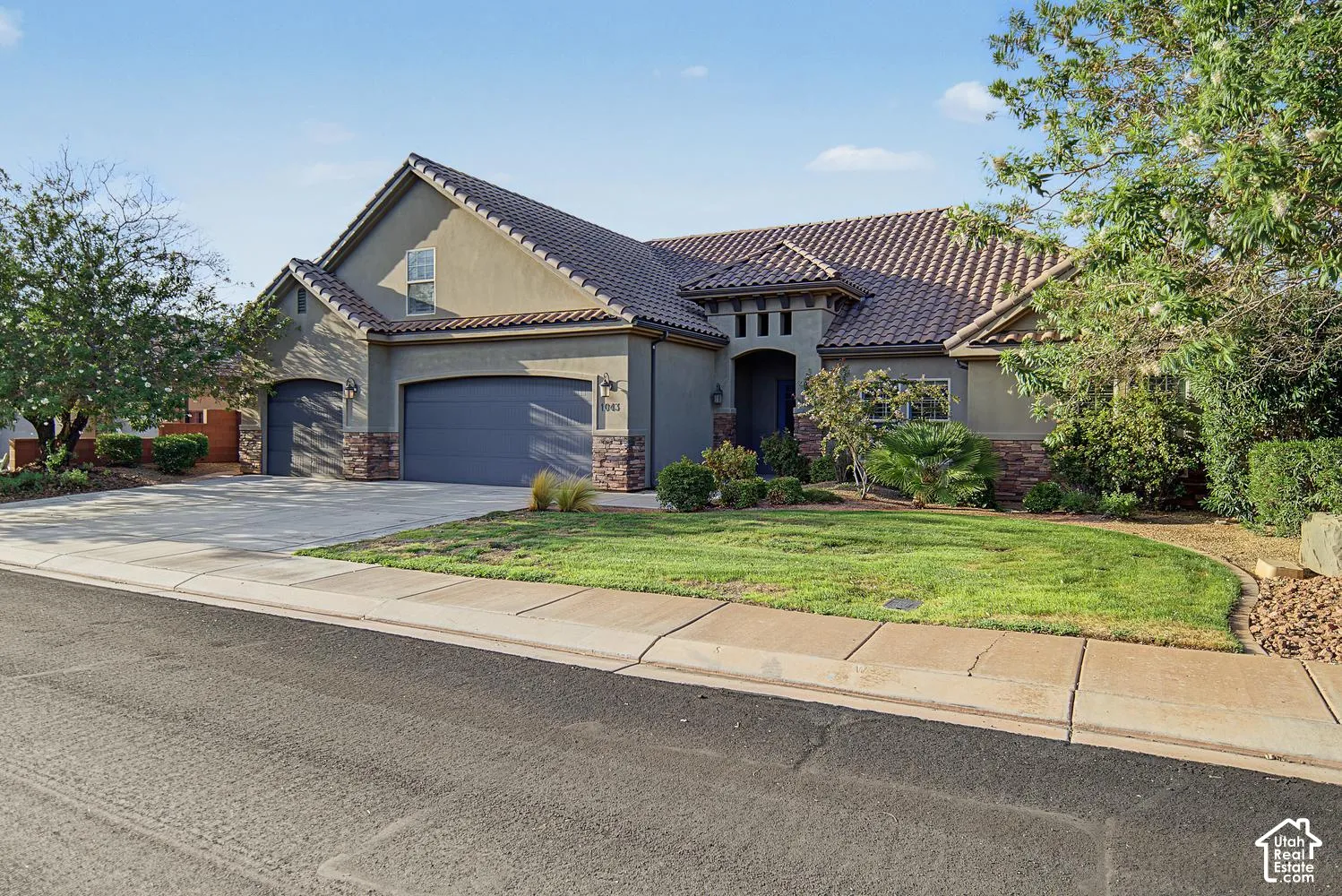 Single-story exterior featuring a tile roof, stucco siding with stone veneer accents, an attached three-car garage, and a landscaped front lawn