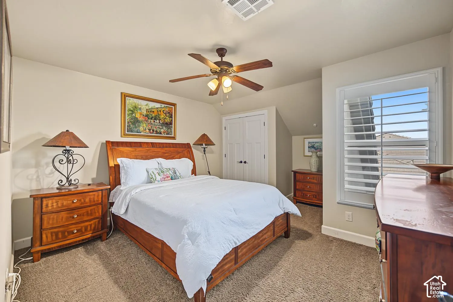 Room featuring neutral wall tones, plantation shutters, a ceiling fan with integrated lighting, carpeted flooring, and double-door closet storage