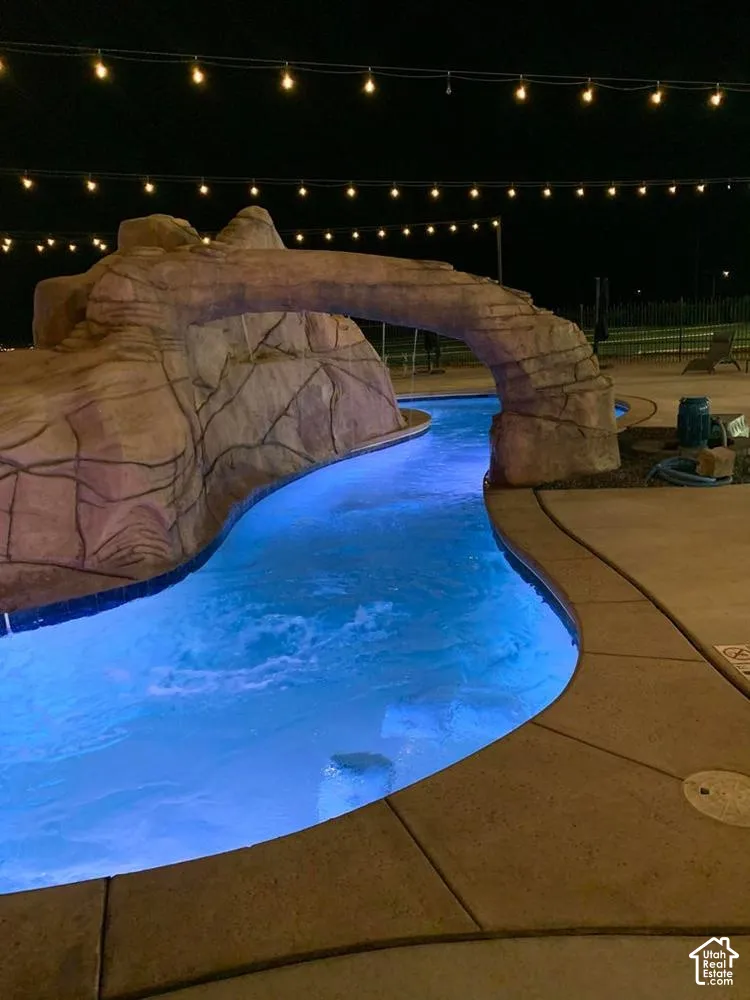 Custom swimming pool featuring a naturalistic rock formation, integrated stone archway, underwater lighting, and concrete pool deck