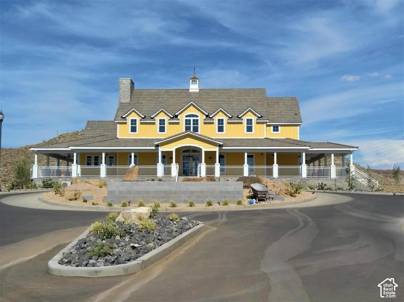 Two-story farmhouse-inspired exterior featuring board-and-batten siding, a wraparound covered porch, multiple dormer windows, a stone-clad chimney, and a cupola