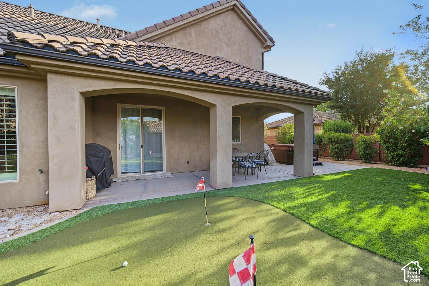 Covered patio featuring stucco columns, tile roofing, an artificial turf putting green, and a manicured lawn