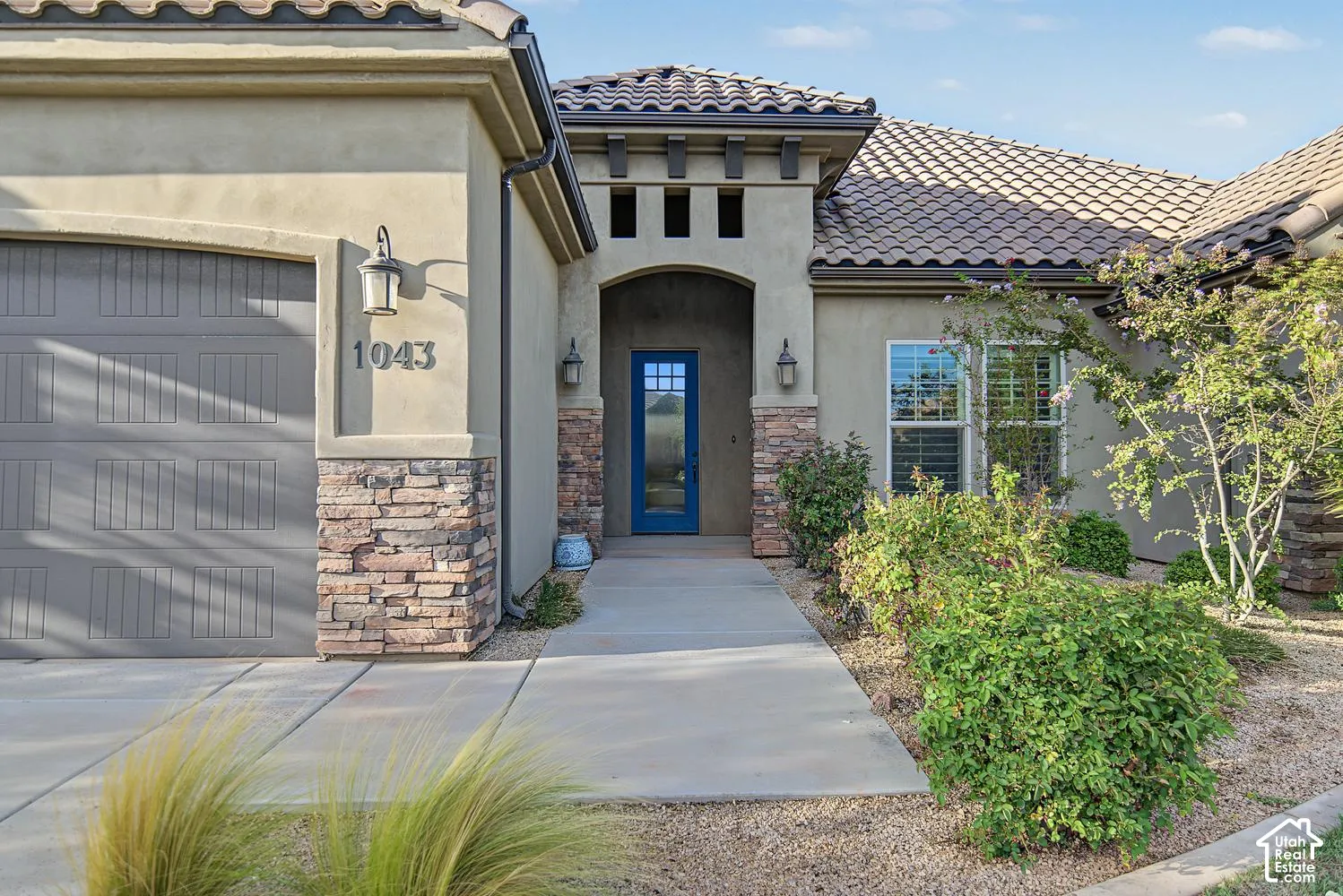 Stucco exterior featuring stacked stone accents, a tile roof, a covered entryway, and a blue front door