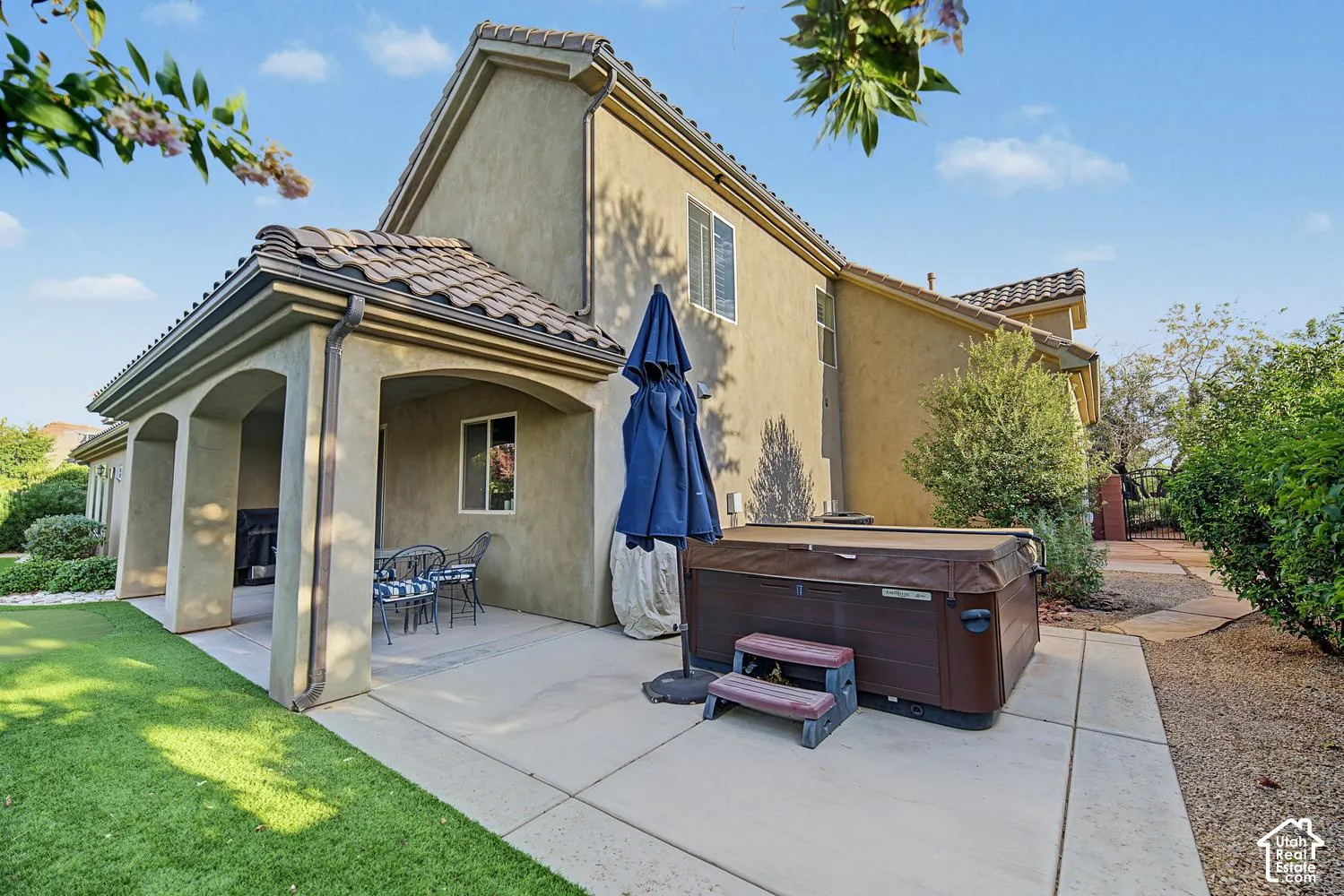 Stucco exterior featuring a covered patio, tile roof, and built-in hot tub situated on a concrete patio