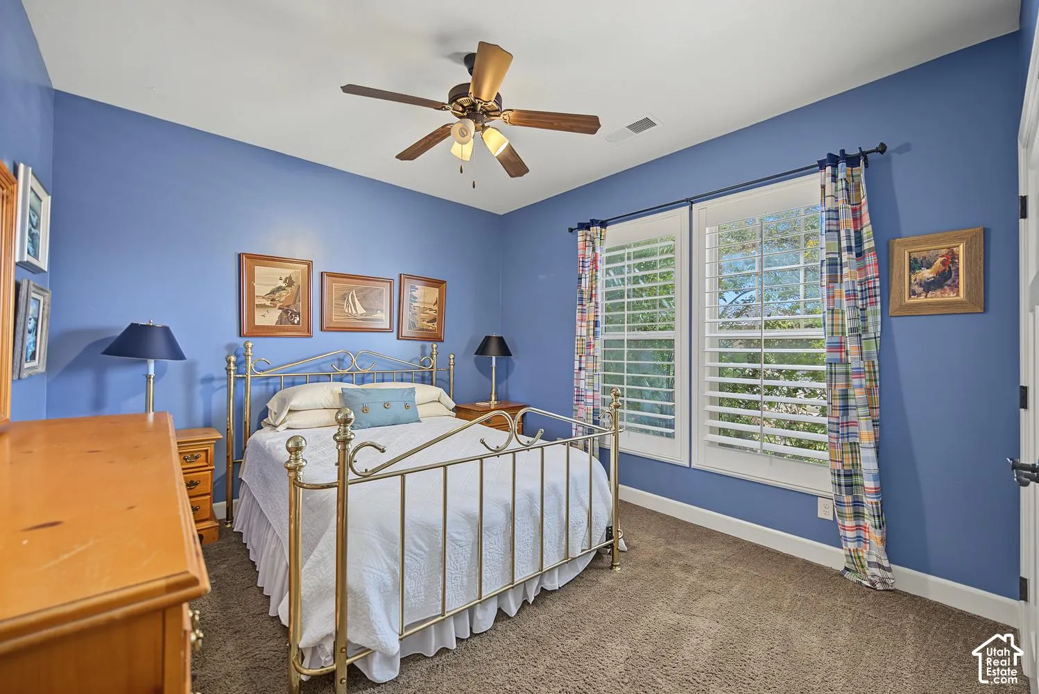 Bedroom featuring wall-to-wall carpeting, dual windows with plantation shutters, and a multi-blade ceiling fan with integrated lighting