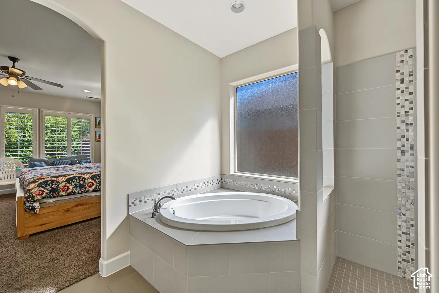 Bathroom featuring a circular soaking tub with a tiled surround, a glass-enclosed shower with decorative accent tile, and a privacy window